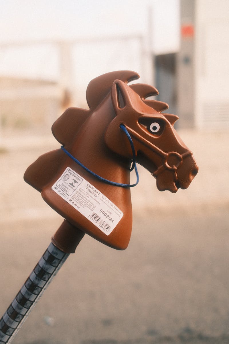 Close-up of a brown toy horse head on a stick outdoors.
